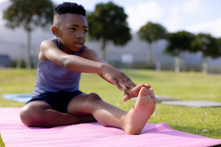 African American child boy stretching forward on pink mat in park, improving flexibility. Exercise, fitness, athletic, wellness, yoga, mobility, balanceの写真素材