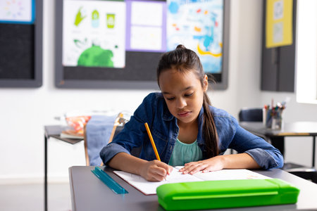 8-year-old girl writing in elementary school classroom, using yellow pencil and teal ruler....
