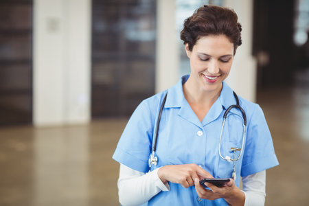 Nurse using on mobile phone with doctors discussing on backgroundの写真素材