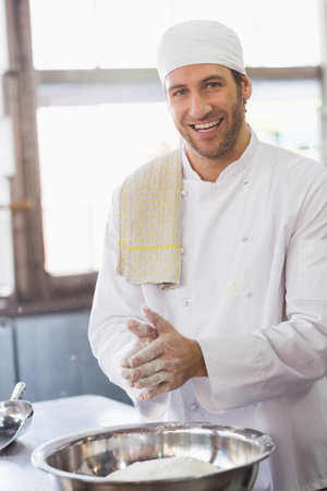 Baker clapping flour from his hands in the kitchen of the bakeryの写真素材