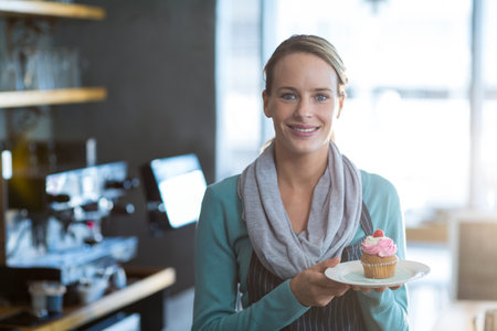 Portrait of smiling waitress holding a plate of cupcake in cafeの写真素材