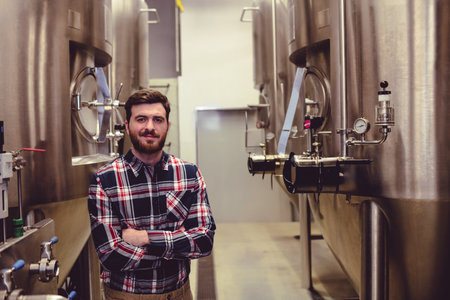 Portrait of confident owner standing with worker amidst machinery at brweeryの写真素材