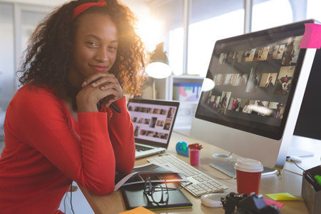 Smiling woman resting chin on clasped hands at modern office desk, with camera and coffee cup. Businesswoman, workspace, contemporary, creative, technology, professional, motivationの写真素材