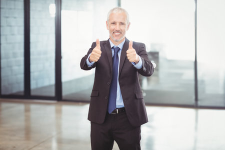 Portrait of businessman giving a thumbs up and businesspeople standing with arms crossed in backgroundの写真素材