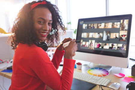 Smiling woman holding stylus pen over graphics tablet in studio workspace, with monitor, copy space. Creative, digital, artist, modern, vibrant, collaborative, innovativeの写真素材