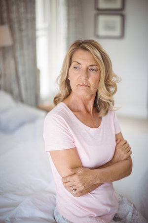 Sitting senior woman crossing arms on bed in bedroom, showing wedding ring, copy space. Retirement, relaxation, serenity, cozy, contemplation, domestic, lifestyleの写真素材