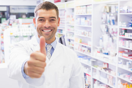 Happy pharmacist holding his thumb at pharmacyの写真素材