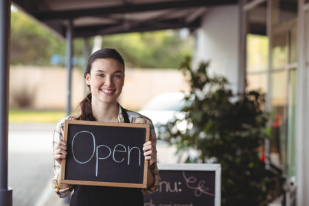 Waiter and waitress standing with chalkboard with open sign outside the cafe
