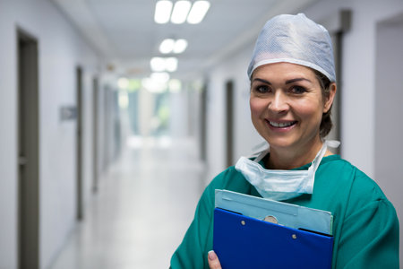 Smiling female surgeon holding blue clipboard and surgical mask in hospital hallway, copy space. Professional, healthcare, medical, clinical, safety, clean, modernの写真素材