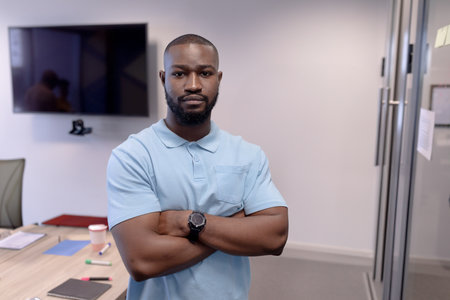 Young African American man standing with crossed arms in modern office, wearing watch, copy space....