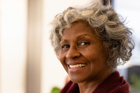 Senior woman smiling in cozy indoor room, radiating gentle warmth and friendly vibes. Warmth, cozy, happiness, indoors, personality, relaxation, comfort, joyの写真素材