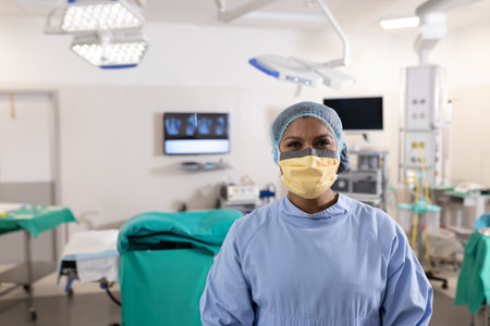 Multiracial female nurse standing in operating room, with overhead surgical lights and equipment....