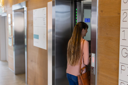 Mid-adult woman standing at open elevator doors in wood-paneled lobby, carrying handbag, copy space....