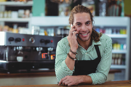 Male barista wearing apron using espresso machine at cafe counter checking smartphone, copy space....