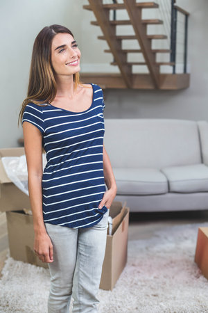 Woman standing in living room near couch and cardboard boxes beside wooden staircase, copy space....