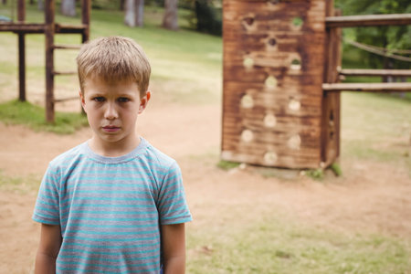 Boy standing on grassy playground near wooden fence and climbing wall with colored handholds....