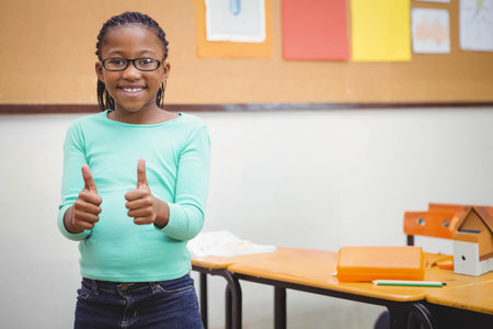 African American girl smiling and holding thumbs up in classroom by wooden student desk, copy space. Cheerfulness, education, youth, learning, academic, confidence, positivityの写真素材