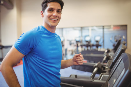 Man jogging on treadmill with digital console at fitness center wearing bright blue athletic tee....