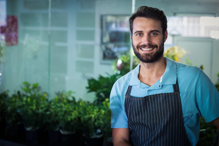 Man wearing striped apron in plant shop smiling at camera among potted plants, copy space....
