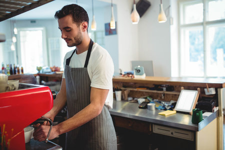 Male barista operating red espresso machine behind wooden counter in coffee shop with knock box. Urban, modern, vibrant, artisanal, hospitality, craftsmanship, workspaceの写真素材