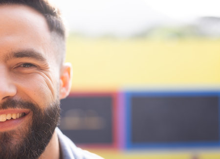 Man smiling while standing in front of yellow cafe wall with colorful boards, copy space. Portrait, male, happiness, vibrant, outdoor, urban, cheerfulの写真素材