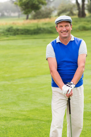 Senior golfer holding club with gloved hands smiling on fairway wearing flat cap. Luxury, leisure, outdoor, nature, recreation, stylish, vibrantの写真素材