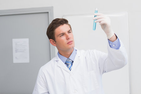 Male laboratory scientist wearing lab coat and latex gloves inspecting blue liquid test tube in lab. Scientist, research, medical, innovation, scientific, technology, diagnosticsの写真素材