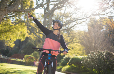 Female cyclist wearing sportswear, helmet and gloves riding bicycle along park path pointing upward. Outdoor, fitness, activity, nature, recreation, adventure, vibrantの写真素材