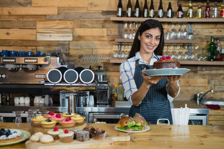 Female barista holding chocolate cake with raspberries at cafe counter with coffee tap, copy space....