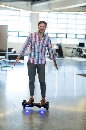 Mid-thirties man balancing on black hoverboard with blue LEDs gliding across modern office floor....