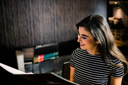Woman holding menu, reading it while sitting at restaurant table with wooden slat wall, copy space....