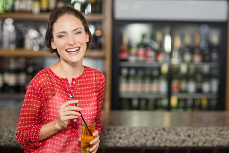 Female patron standing at bar counter holding glass of drink near refrigerated display, copy space. Socializing, beverage, hospitality, relaxation, casual, interior, modernの写真素材