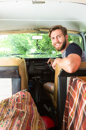 Man sitting in vintage camper van turning toward camera with action camera in forest, copy space....
