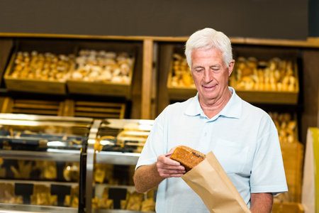 Senior man wearing polo shirt placing seeded loaf into paper bag at bread display, copy space....