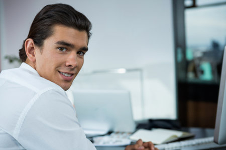Man in his 30s turning head and torso at office desk with computer monitor, copy space. Business, professionalism, workspace, modern, productivity, technology, corporateの写真素材