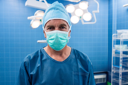 Senior male surgeon in scrubs standing in operating room with surgical lights checking supply cart. Medical, healthcare, clinical, surgical, hospital, professionalism, sterileの写真素材