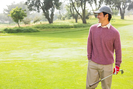 Golfer standing on fairway wearing gray cap and red glove and holding golf club near trees. Outdoor, leisure, sport, technique, relaxation, landscape, apparelの写真素材