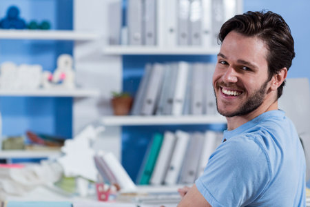 Man turning back at desk in bright workspace holding coffee mug and geometric model, copy space. Office, productivity, modern, minimalist, workspace, professional, organizationの写真素材