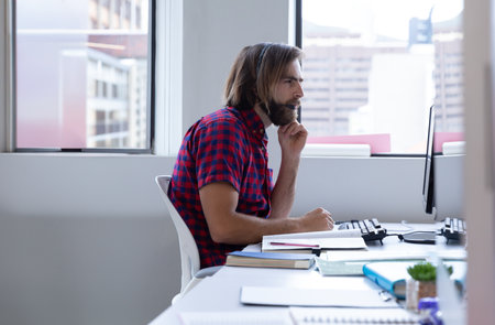 Male office worker looking intently at computer monitor at desk in modern office with succulent....