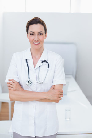 Middle aged female doctor wearing tunic and stethoscope standing in exam room by exam table. Medical, healthcare, professionalism, clinical, diagnostic, wellness, cleanの写真素材