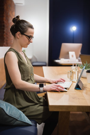 Female professional typing on tablet with keyboard, coffee cup at office by brick wall, copy space. Workspace, technology, modern, productivity, sedentary, corporate, leisureの写真素材