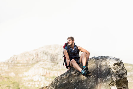Male hiker sitting on boulder on rocky hillside wearing hiking backpack and trail shoes and smiling. Adventure, exploration, outdoor, rugged, nature, trekking, leisureの写真素材