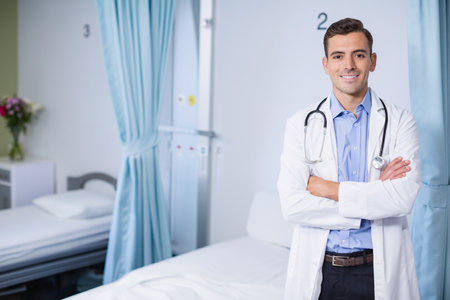 Male physician standing by hospital ward bed monitoring panel with stethoscope, copy space. Medical, healthcare, wellness, professionalism, clinical, outpatient, diagnosticの写真素材