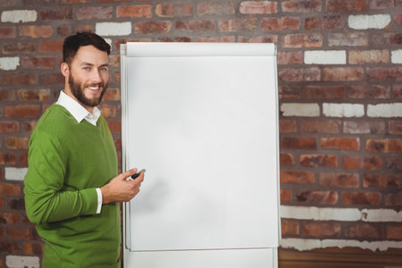 Man standing next to flipchart easel holding marker over blank pad against brick wall, copy space. Professional, presentation, creative, training, workshop, education, urbanの写真素材