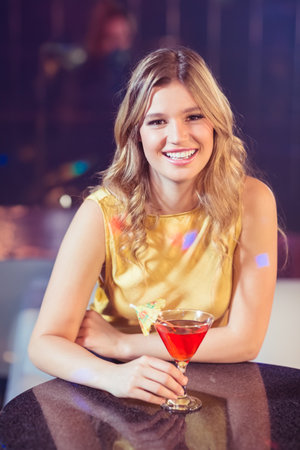 Woman sipping red cocktail from martini glass with umbrella garnish at table in dimly lit bar. Elegant, nightlife, glamour, sophistication, leisure, ambiance, trendyの写真素材