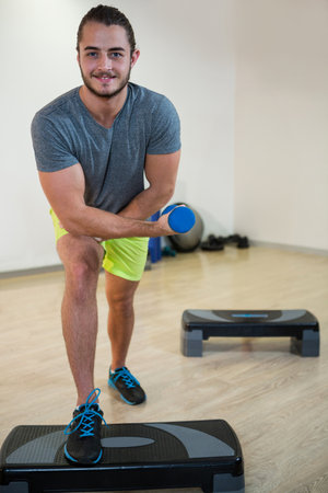 Male exerciser in sportswear performing lunge curl on platform in fitness studio with blue dumbbell. Athletic, strength, workout, fitness, training, minimal, modernの写真素材