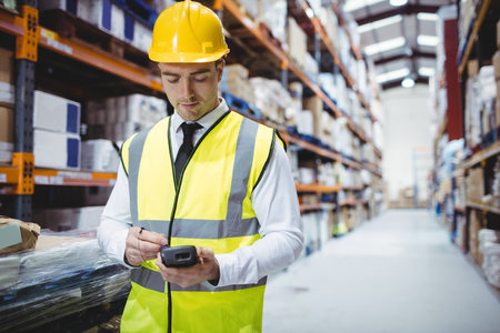 Adult male wearing hard hat scanning boxes in warehouse aisle using handheld scanner, copy space....