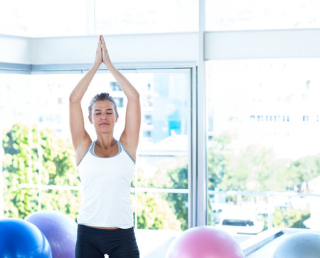 Woman wearing white tank top, black leggings practicing yoga in studio with colorful exercise balls. Fitness, wellness, posture, inspiration, interior, natural light, mindfulnessの写真素材
