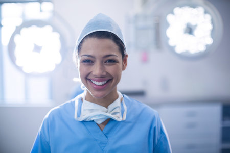 Female surgeon standing in bright surgical suite under overhead lights wearing blue scrubs and mask. Medical, healthcare, clinical, professionalism, sterile, clean, modernの写真素材