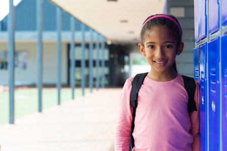 Backpack is leaning against blue metal lockers in covered outdoor school corridor overlooking grass. Child, education, schoolyard, outdoor, youth, learning, campusの写真素材